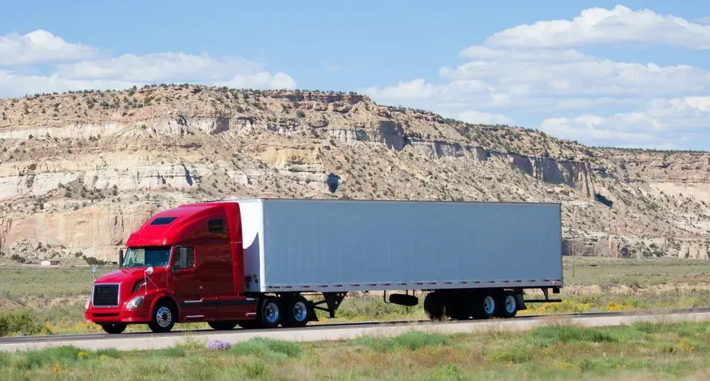 A Red Semi-Truck Driving on a Road in a Desert Landscape — Tamworth Tilt Trays in Tamworth, NSW
