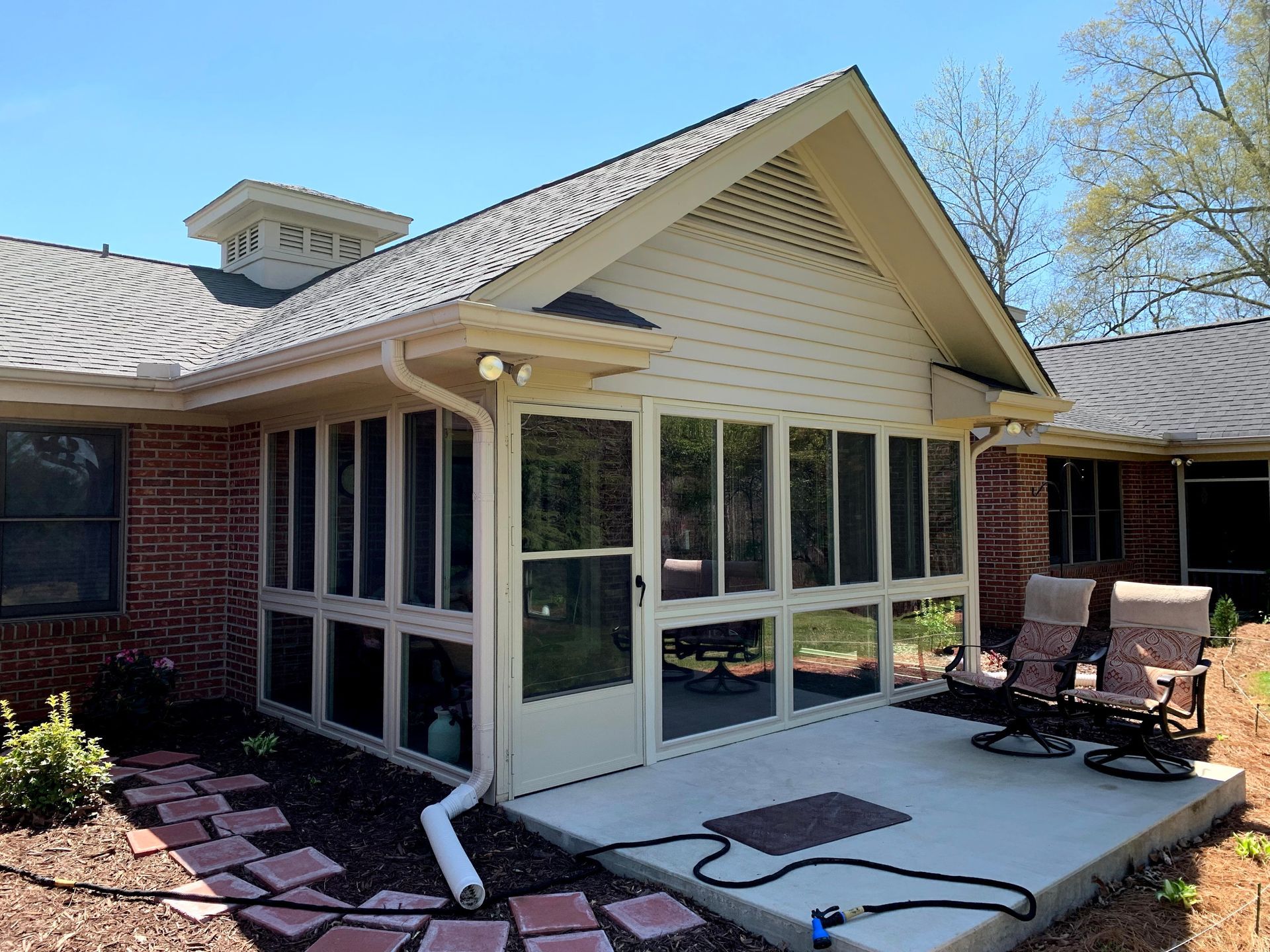 A screened in porch with chairs and a hose in front of a brick house.