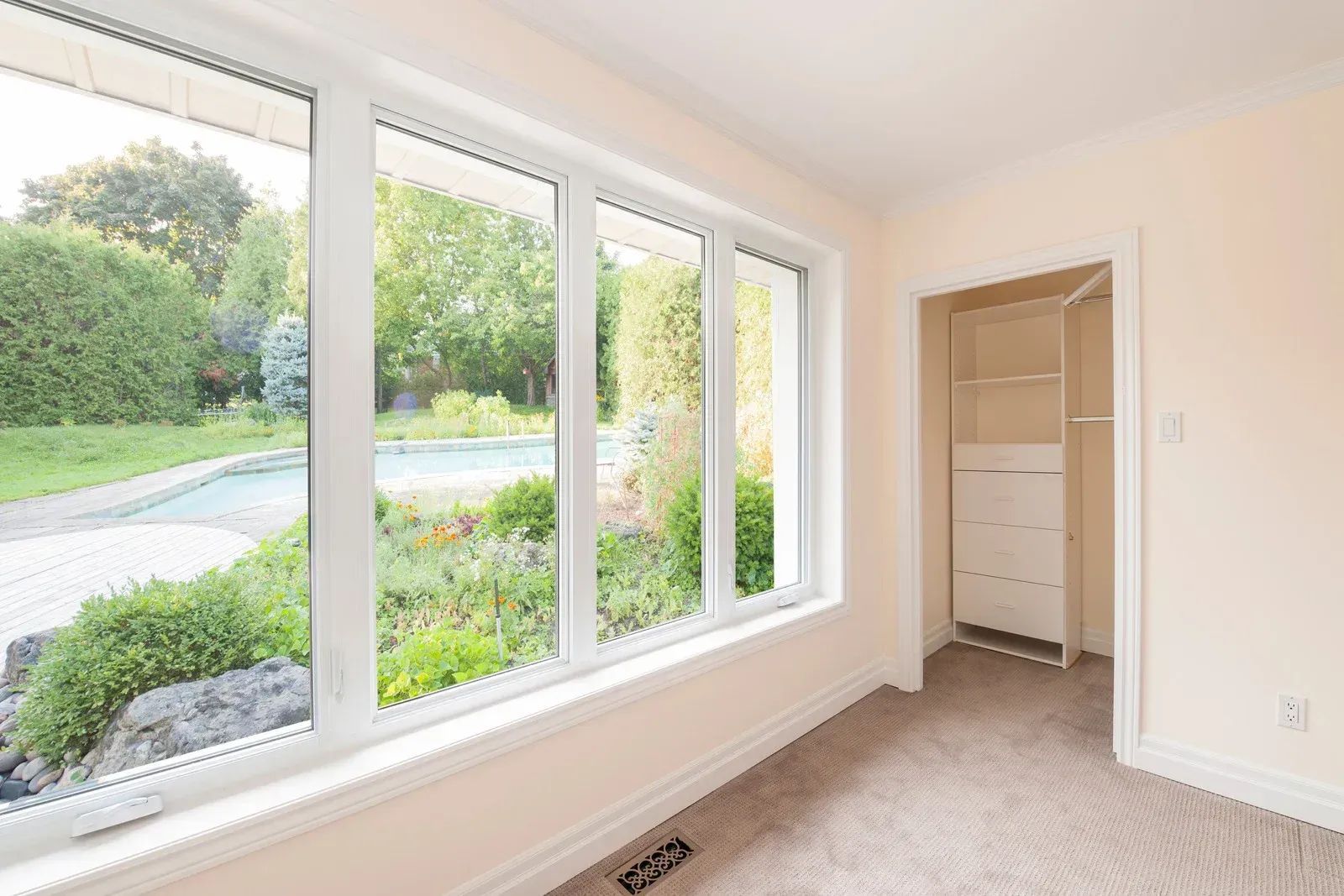 White bay window with view of a park and buildings. A cactus in an orange pot sits inside the window.