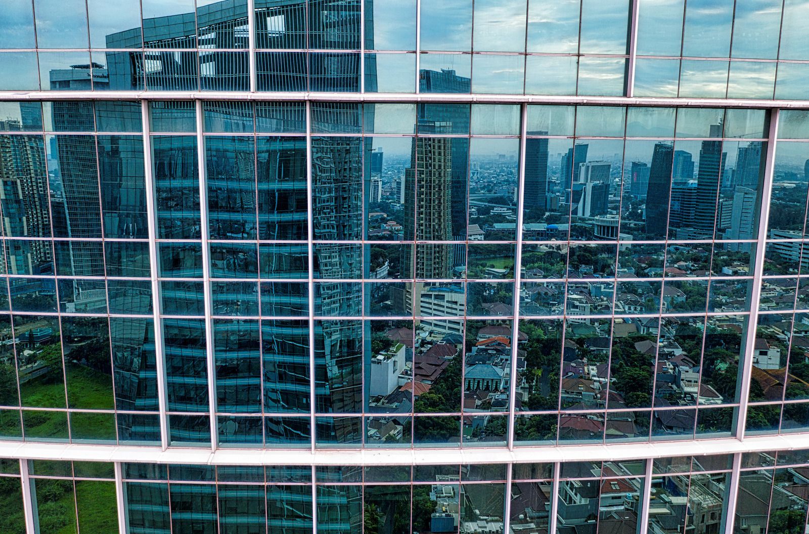Blue-tinted glass building reflecting a cityscape with other high-rise structures in the distance under a cloudy sky.