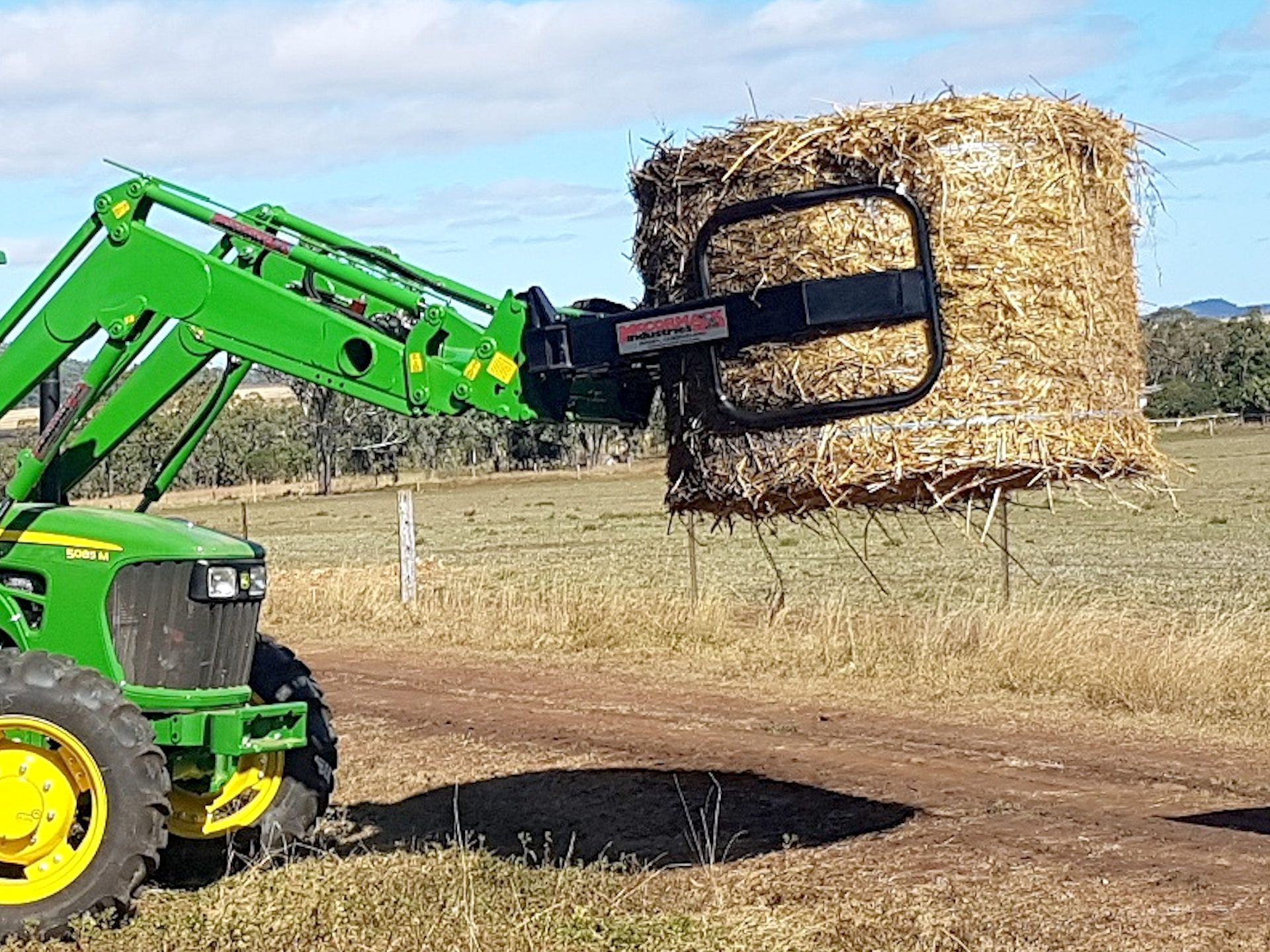 A green tractor is lifting a bale of hay in a field.