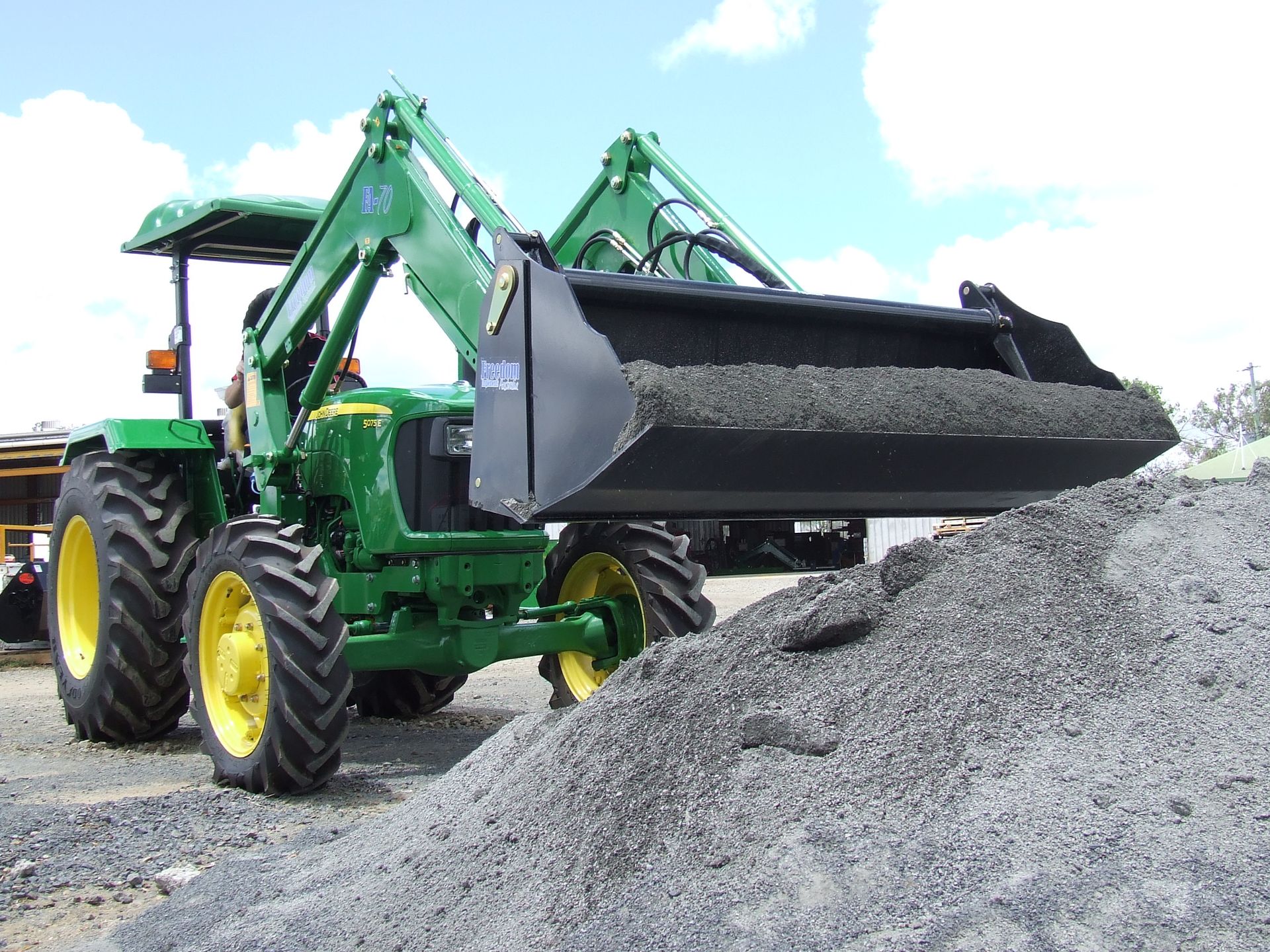 A green john deere tractor with a bucket full of gravel