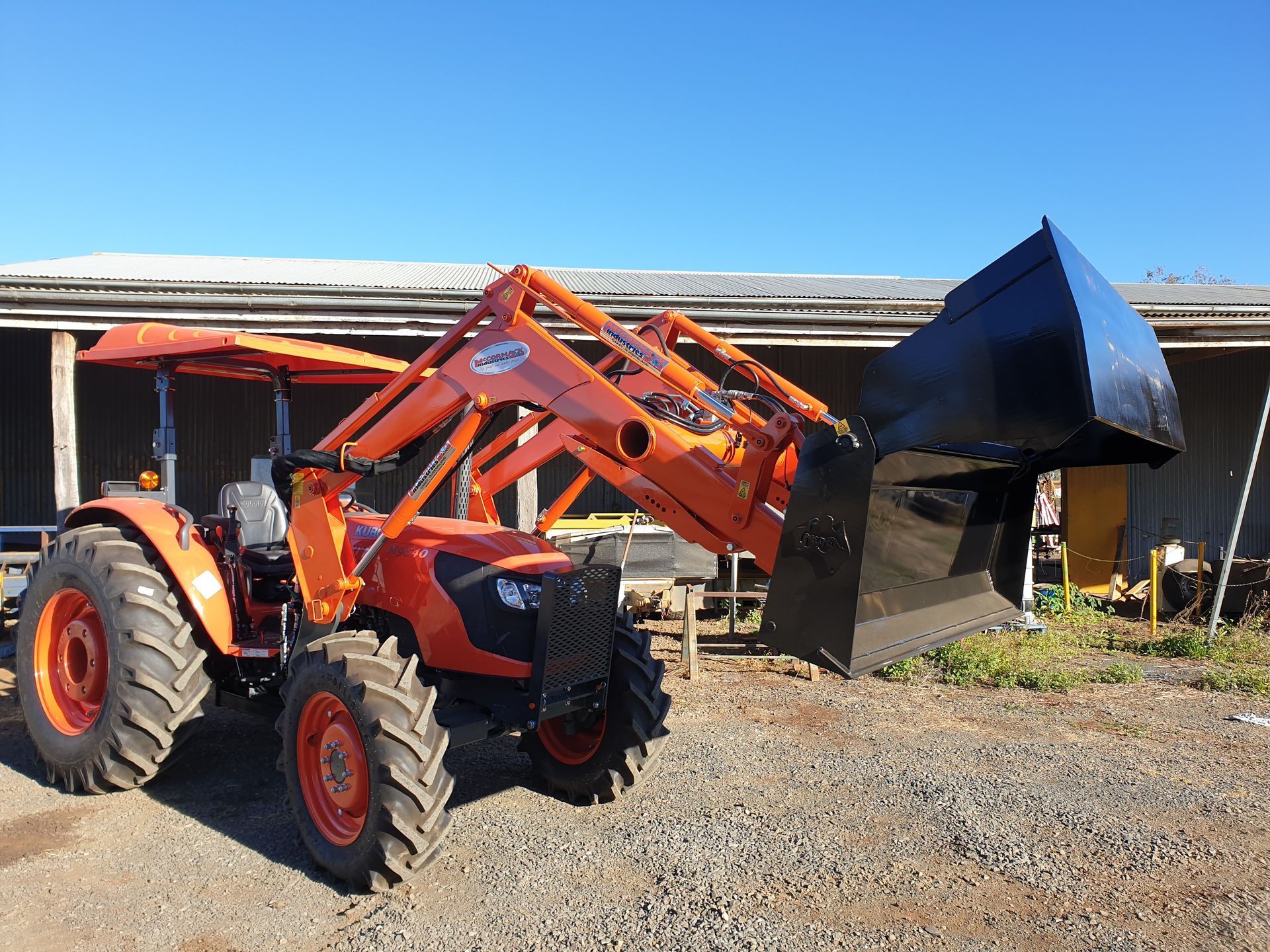 An orange tractor with a black bucket is parked in front of a building.