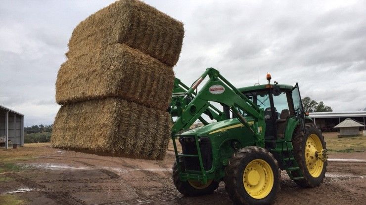 A green tractor is carrying a stack of hay bales.