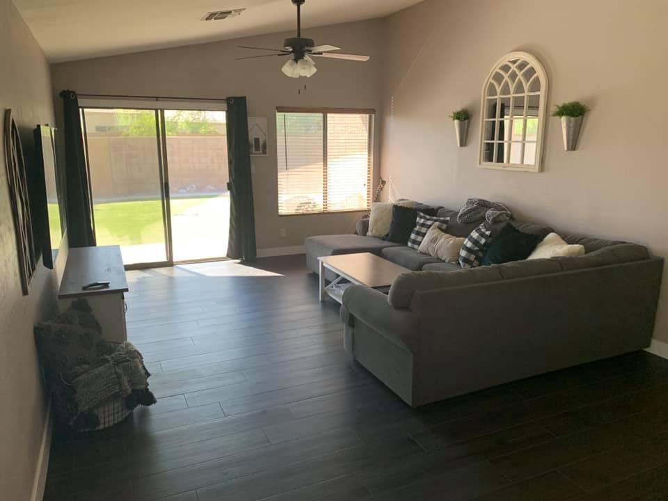 Bright living room with dark floors, gray sectional sofa, TV stand, and sliding glass doors to a backyard.