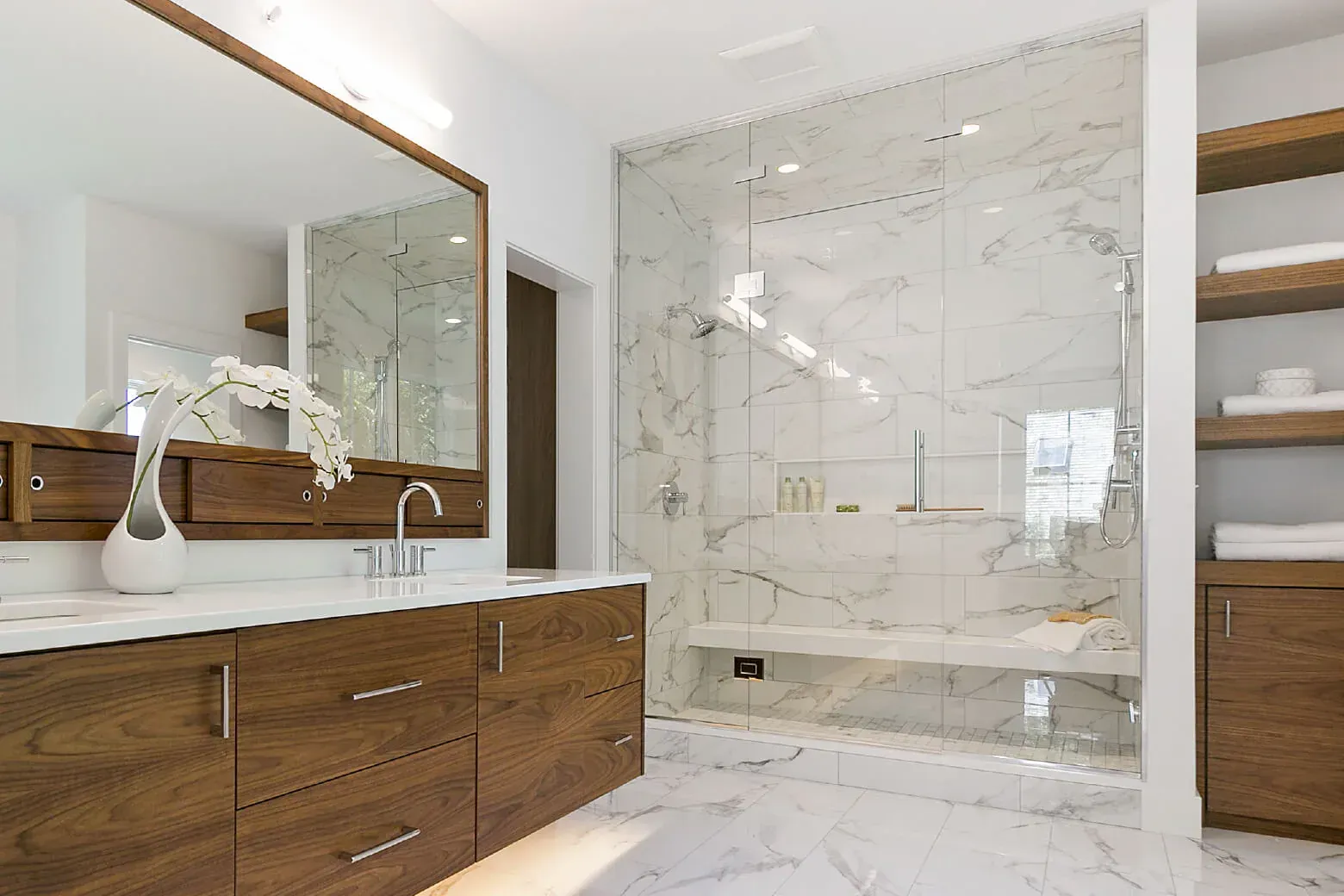 Modern bathroom with wood vanity, large mirror, and glass shower with marble tile