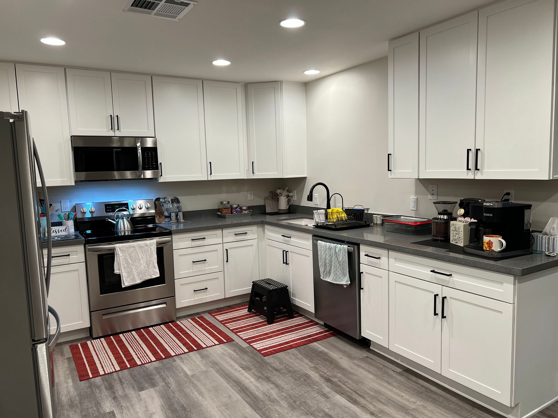 Modern white kitchen with stainless steel appliances, black countertops, and red striped rugs
