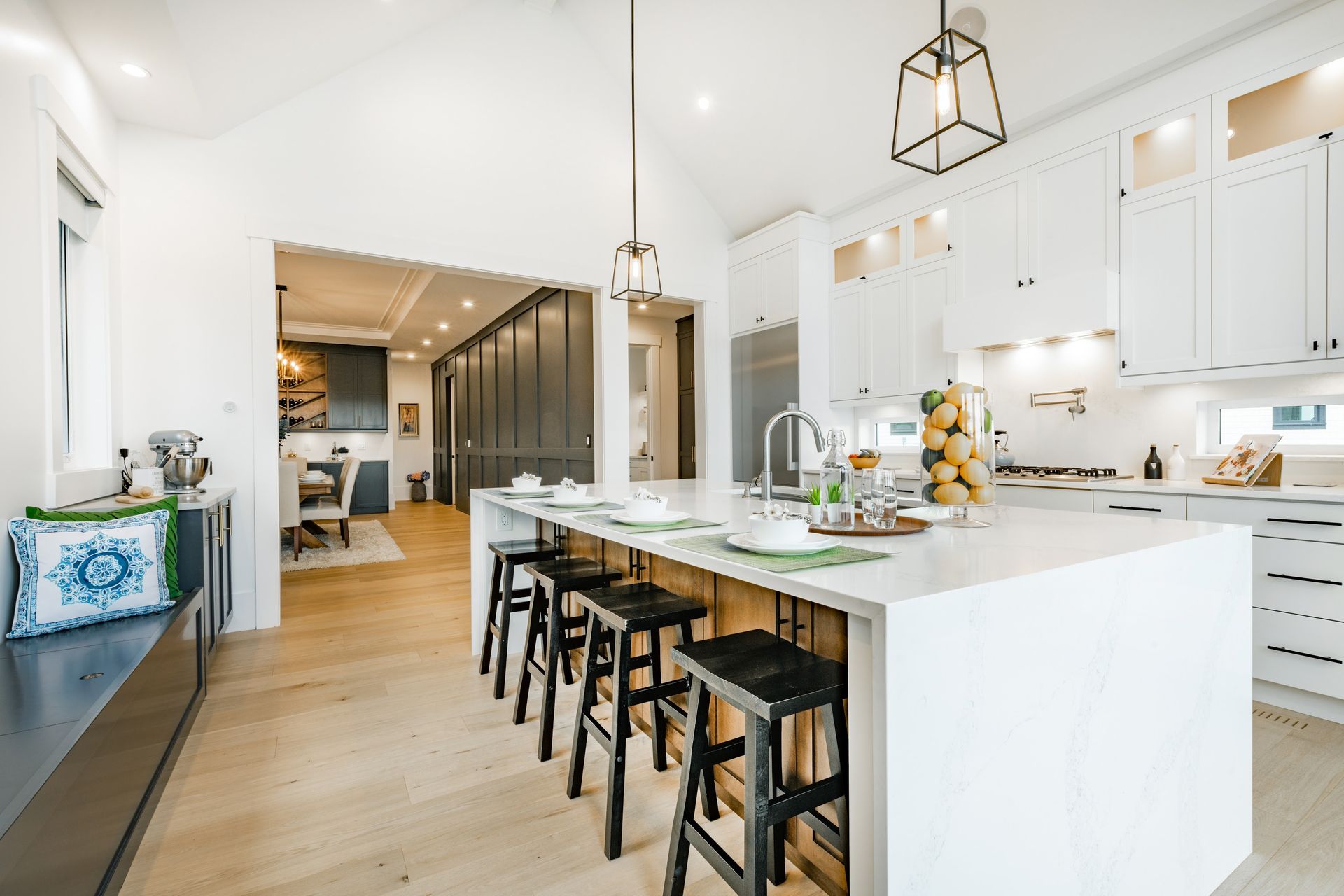 Bright modern kitchen with white island, black stools, pendant lights, and wood floors