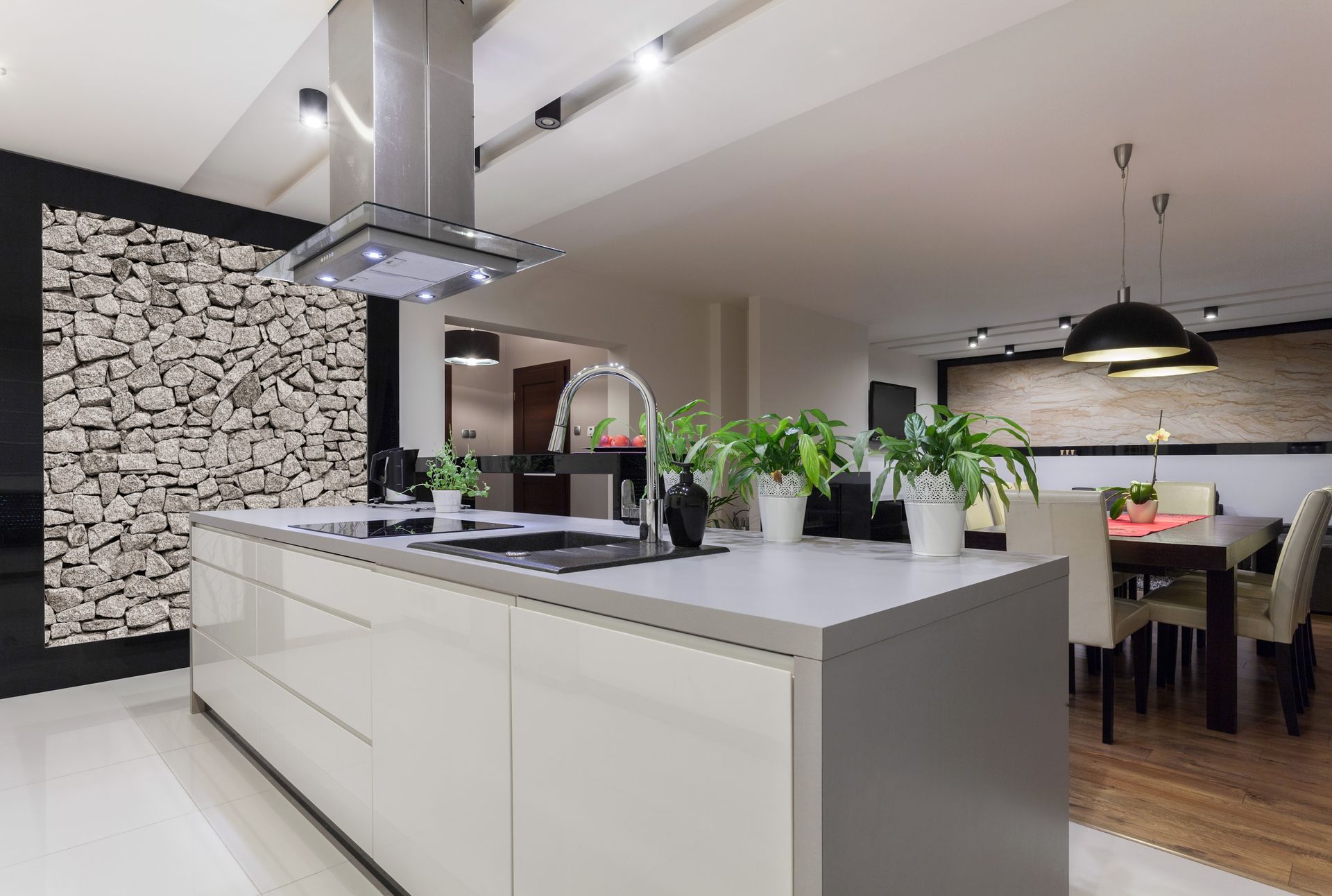 Modern kitchen with white island, stainless range hood, potted plants, and dining area in the background