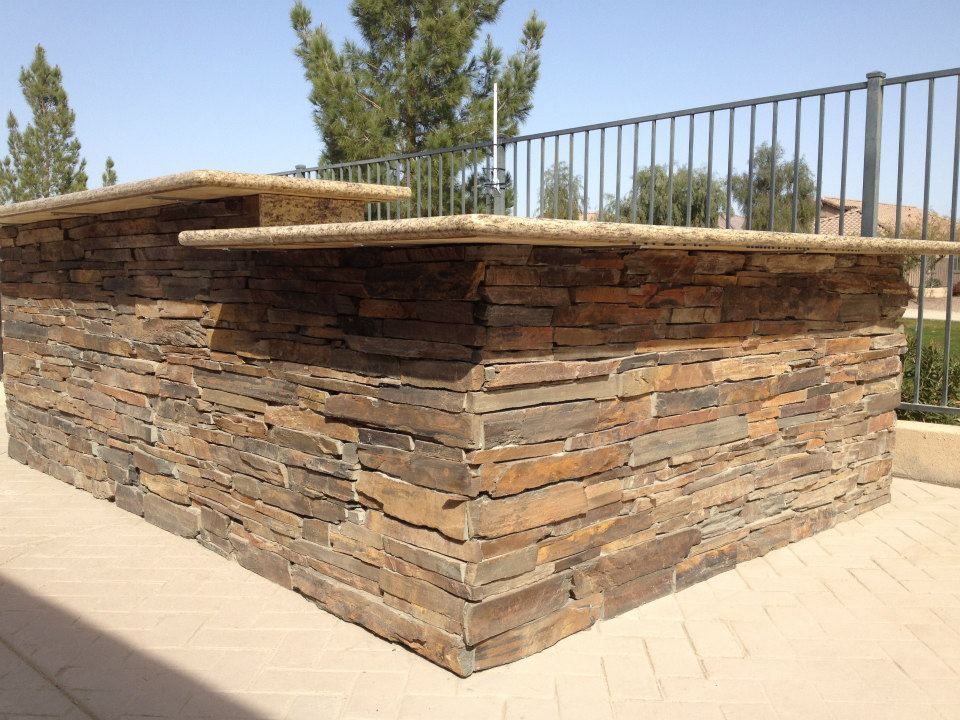 Stone outdoor bench with a flat top on a paved patio near a black metal fence