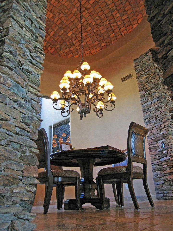 Stone-walled dining nook with round table, chairs, and ornate chandelier under a tiled dome ceiling