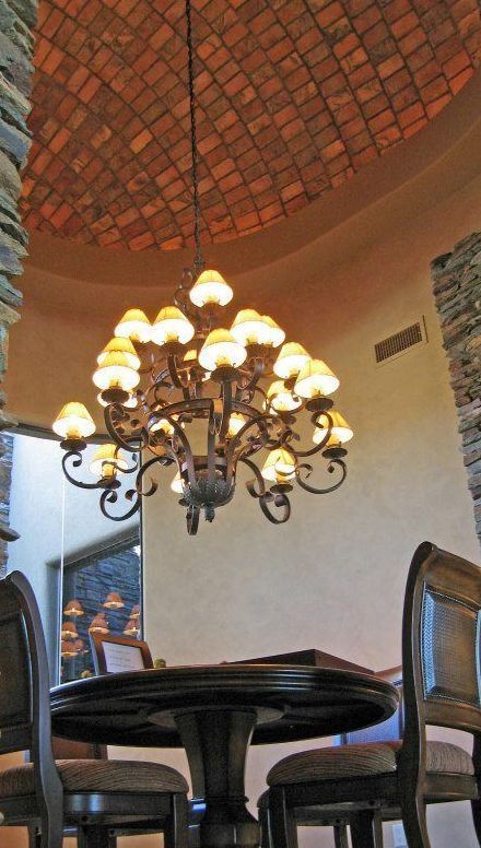 Elegant chandelier above a dark table and chairs in a room with a tiled domed ceiling