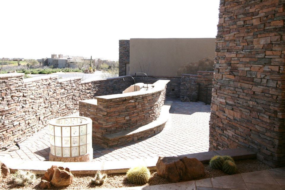 Stone patio with curved walls and built-in seating beside a brick building in bright sunlight