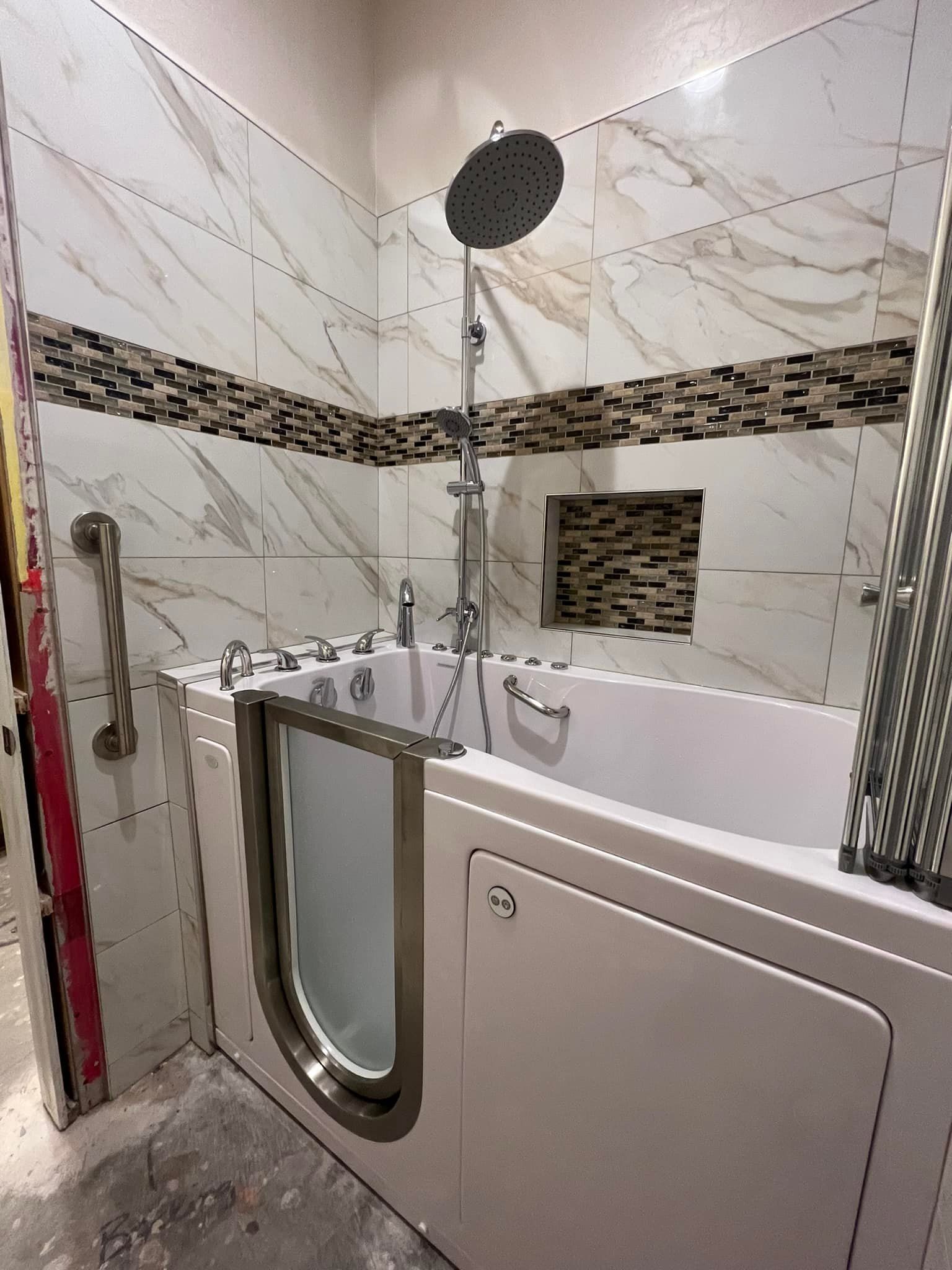 Accessible bathroom with a walk-in tub, showerhead, grab bars, and marble tile walls.