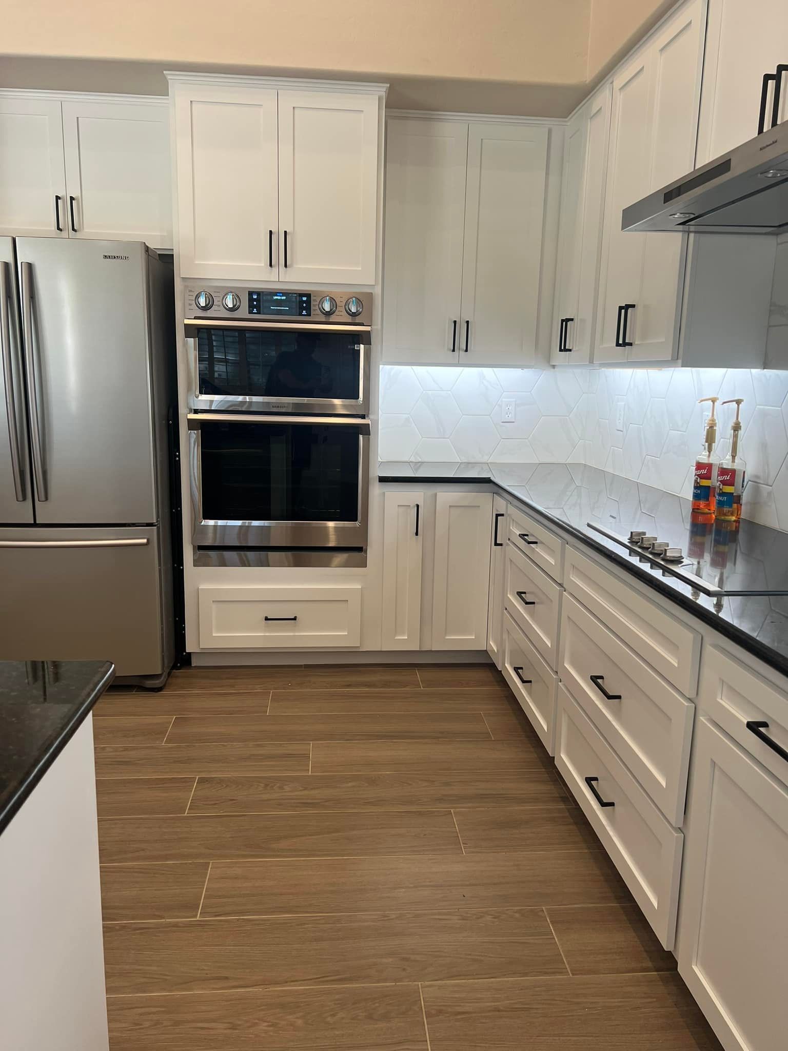 Modern kitchen with stainless steel appliances, white cabinets, dark countertops, and wood-look flooring