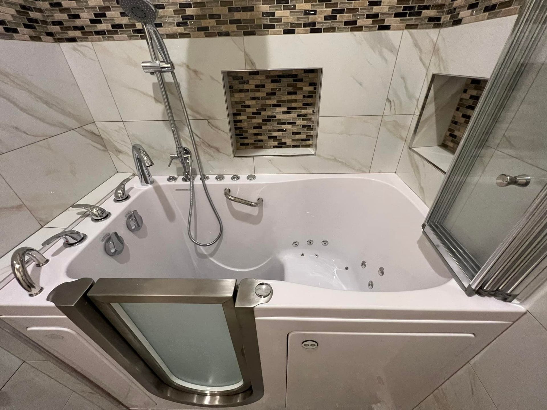 Corner bathtub with chrome fixtures, handheld shower, glass door, and beige tile bathroom wall.