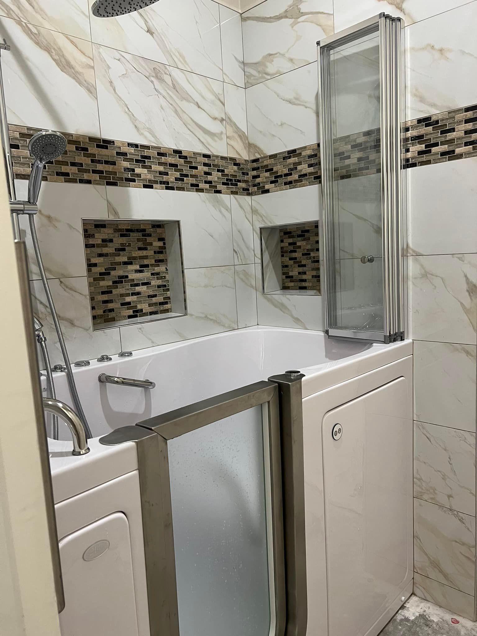 Bathroom with walk-in tub, glass shower door, and beige tiled walls with mosaic accents.