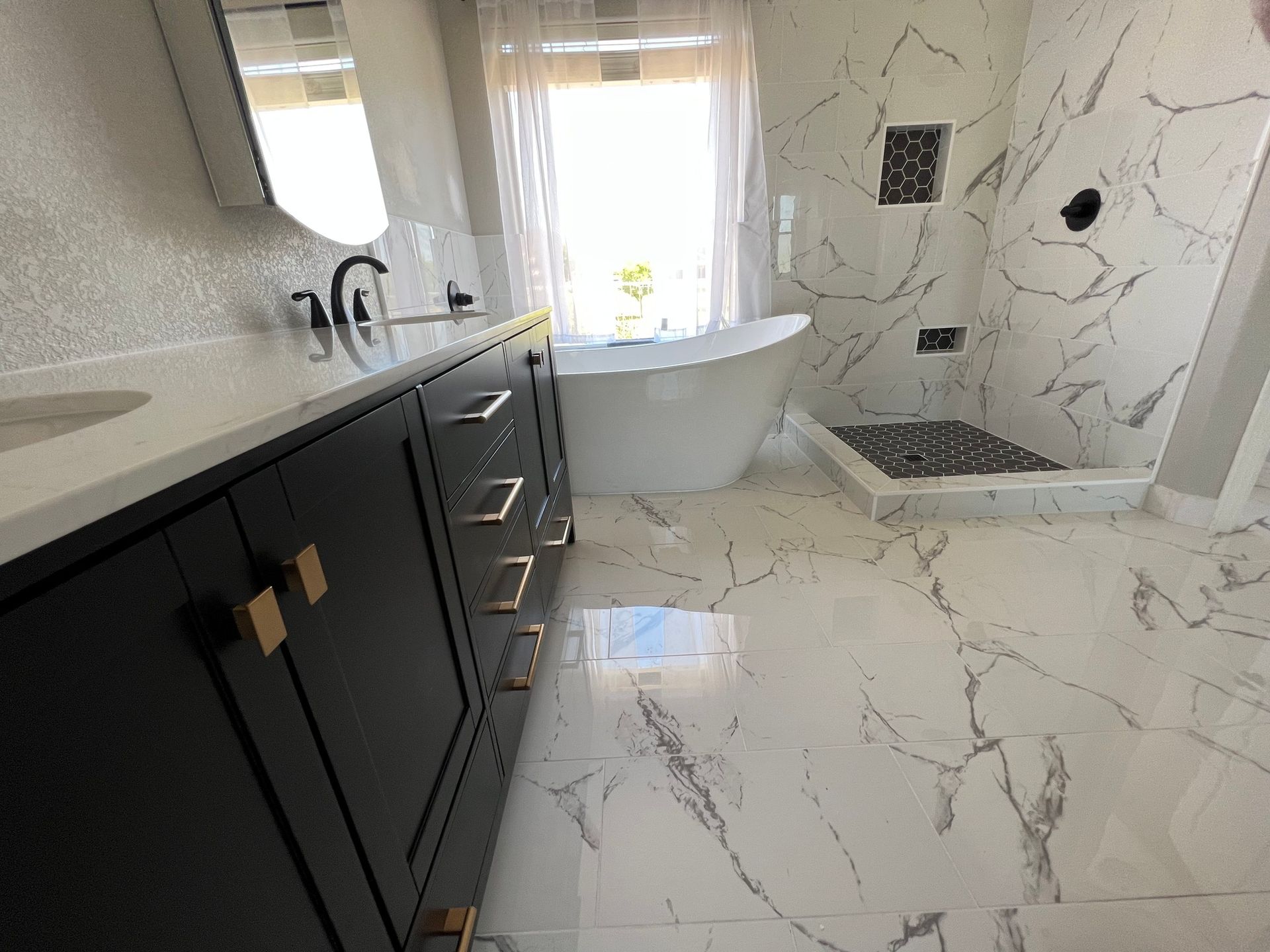 Modern bathroom with black vanity, white marble tile, freestanding tub, and walk-in shower