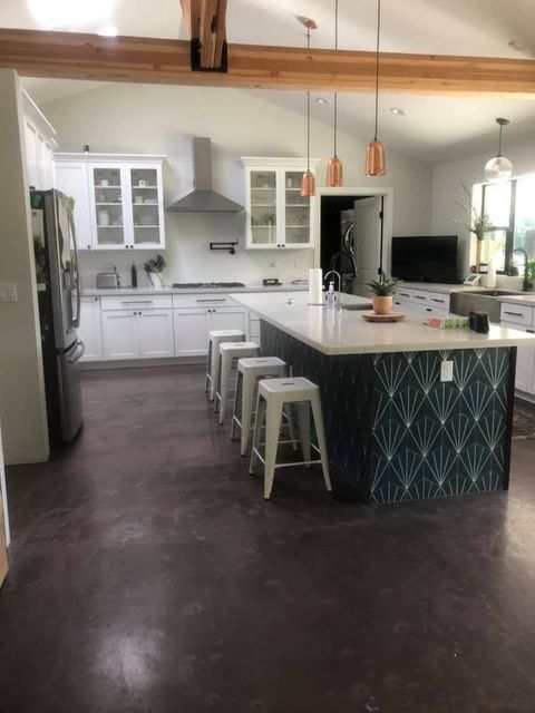 Bright modern kitchen with white cabinets, marble island, black appliances, and gray wood flooring