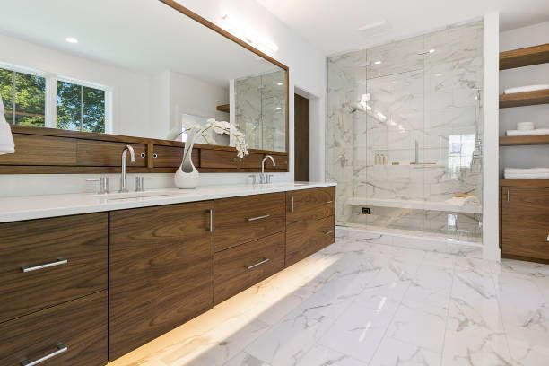 Modern bathroom with wood vanity, double sinks, large mirror, and glass-enclosed shower with white marble tile