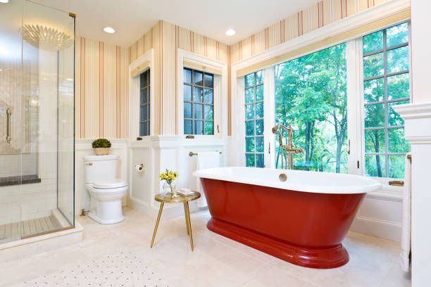 Bright modern bathroom with red clawfoot tub, large windows, glass shower, and white toilet