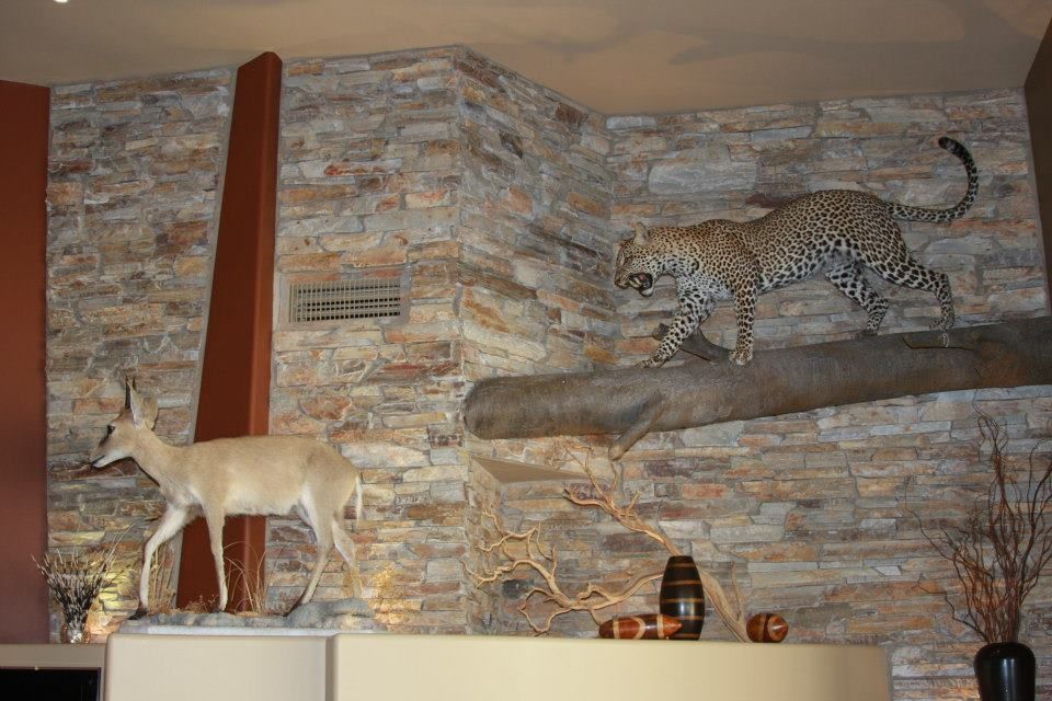 Stone fireplace display with mounted leopard, deer statue, and decorative branches