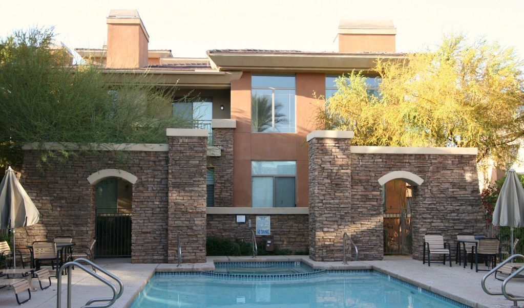 Apartment courtyard with a swimming pool, brick buildings, and trees in warm sunlight