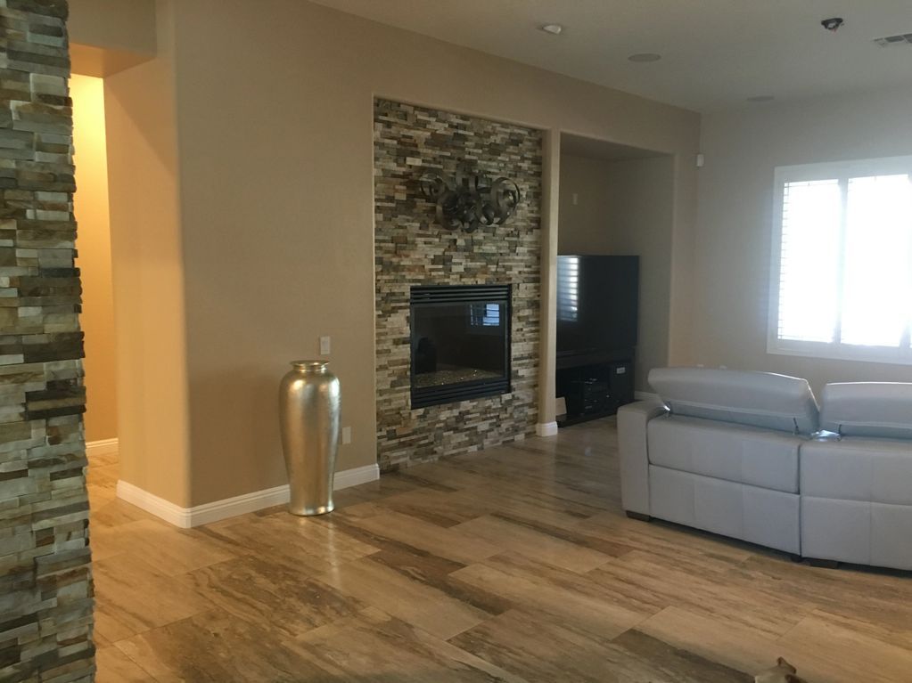 Modern living room with stone fireplace, wood floor, gray sectional, and bright window.
