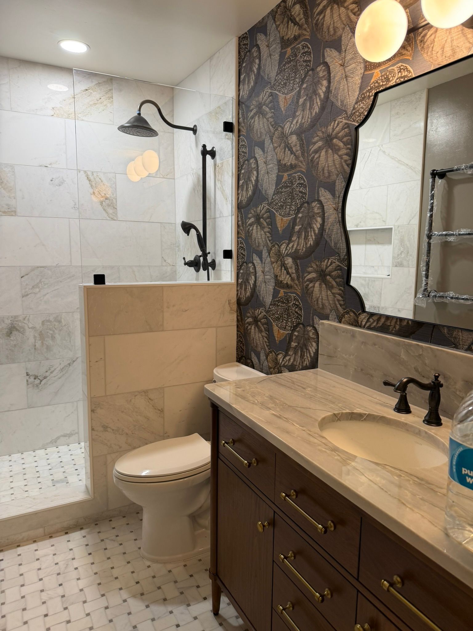 Modern bathroom with walk-in shower, marble vanity, dark cabinets, and patterned accent wall.