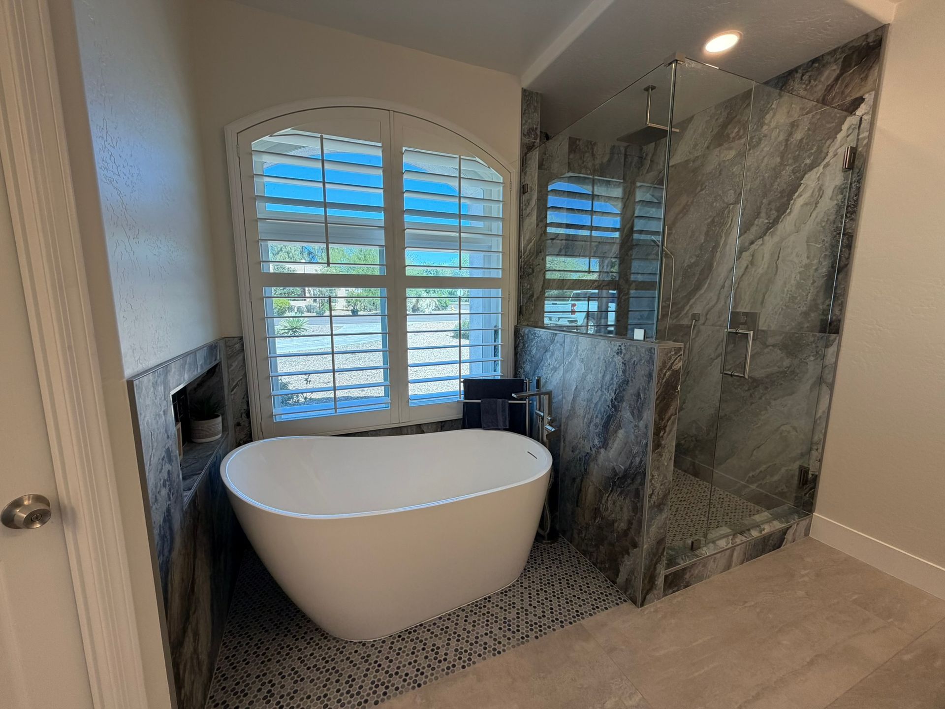 Modern bathroom with freestanding tub, marble walk-in shower, and window shutters