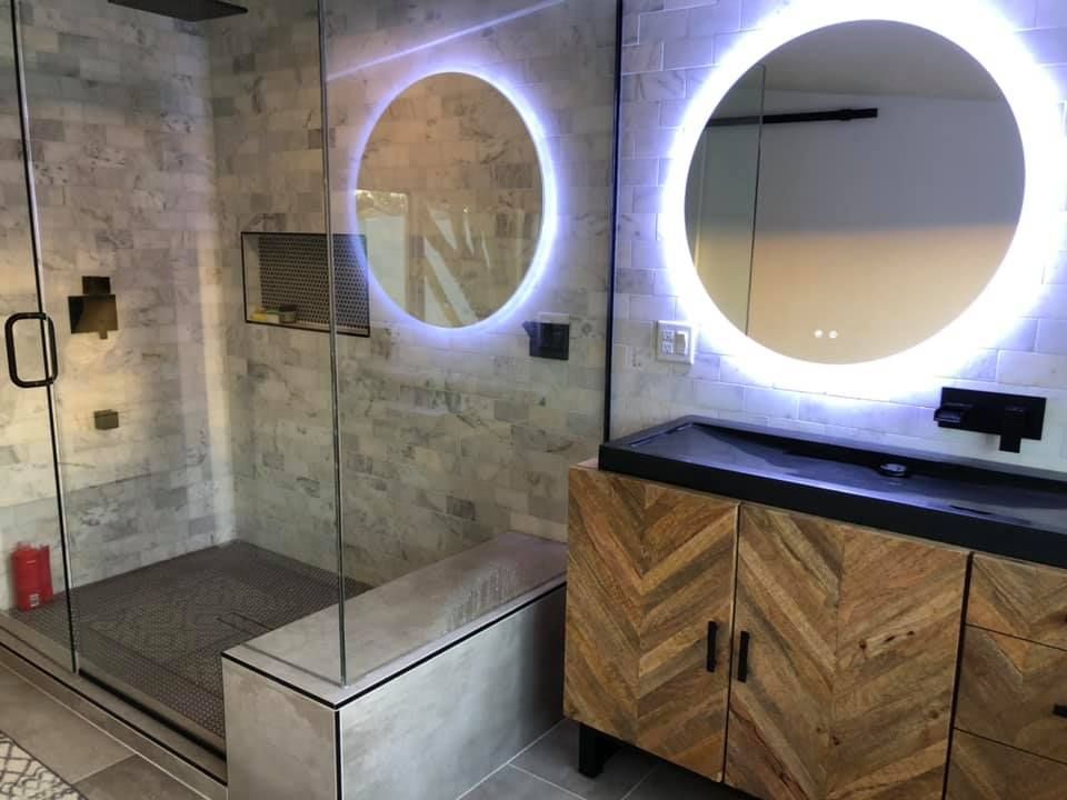 Modern bathroom with glass shower, round backlit mirror, and wood vanity cabinet