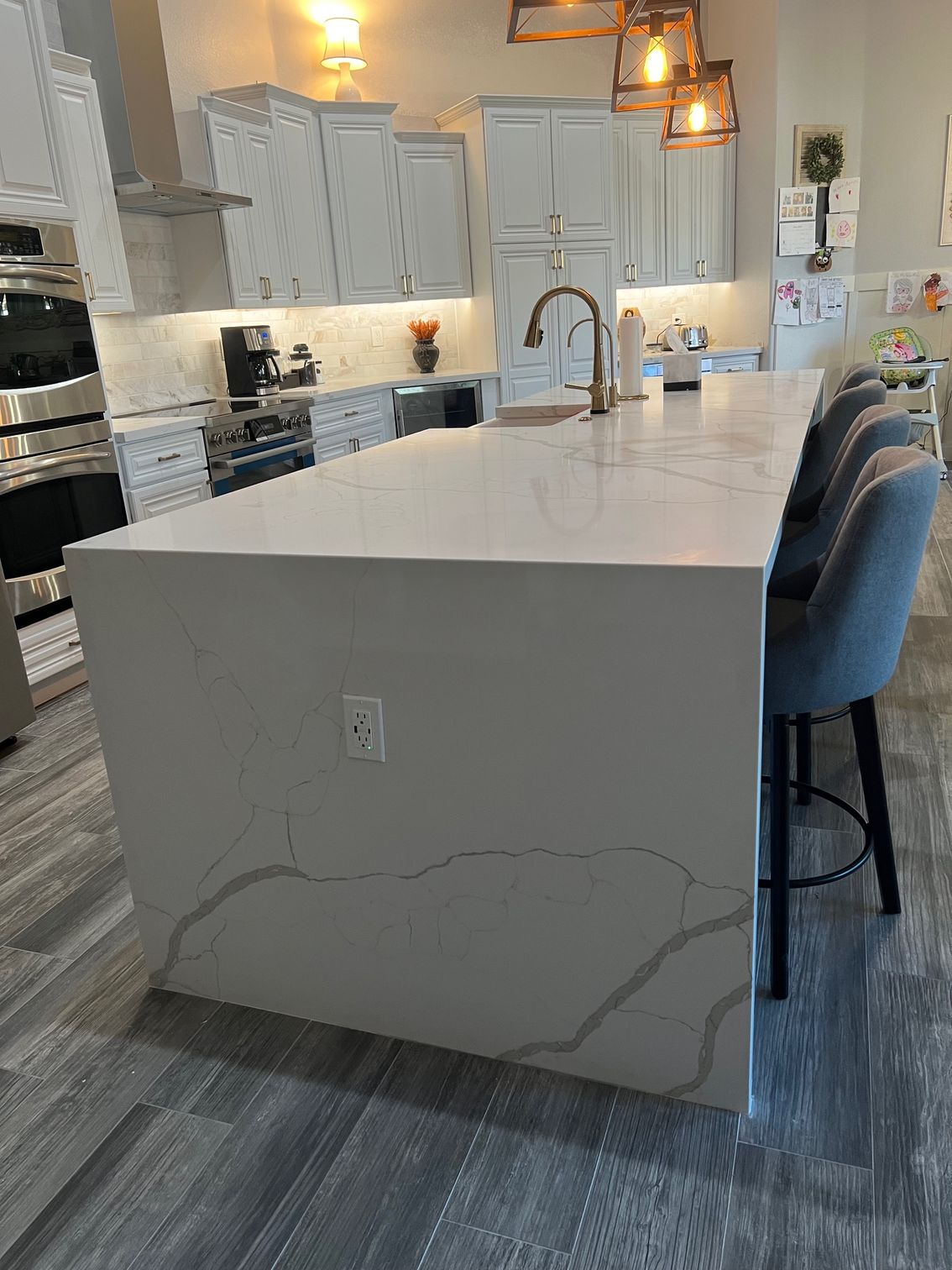 Modern kitchen with large white island, gray cabinets, pendant lights, and bar stools