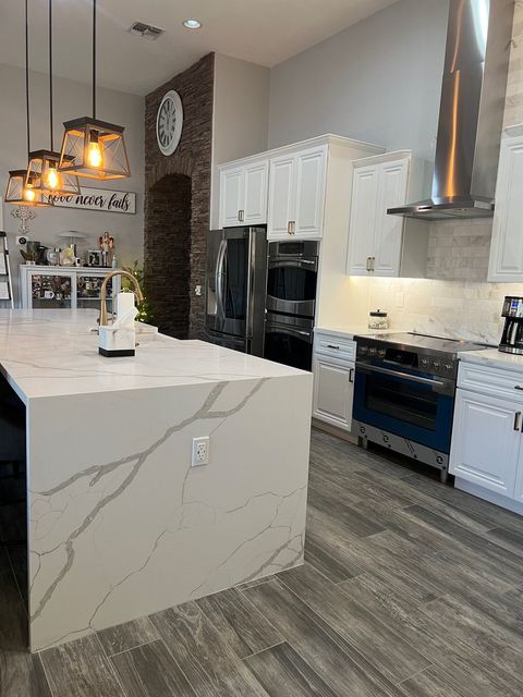 Bright modern kitchen with white cabinets, marble island, black appliances, and gray wood flooring