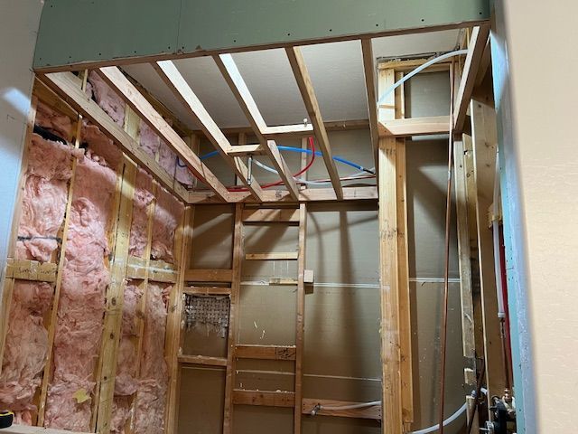 Unfinished bathroom framing with exposed studs, insulation, and ceiling joists during renovation.
