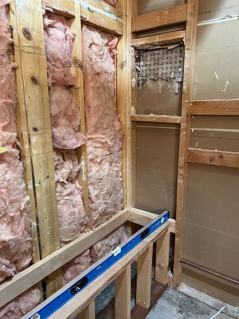 Unfinished bathroom wall framing with pink insulation, exposed studs, and a level on a wood support.