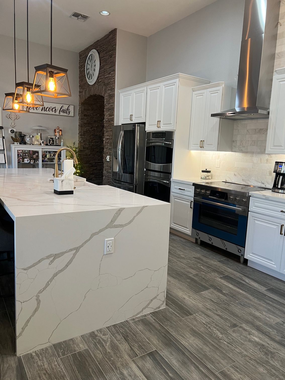 Modern kitchen with marble island, white cabinets, stainless appliances, and wood-look flooring