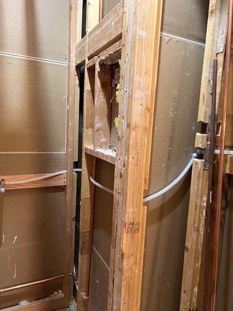 Exposed wooden wall framing and drywall in a narrow construction area with a curved white pipe