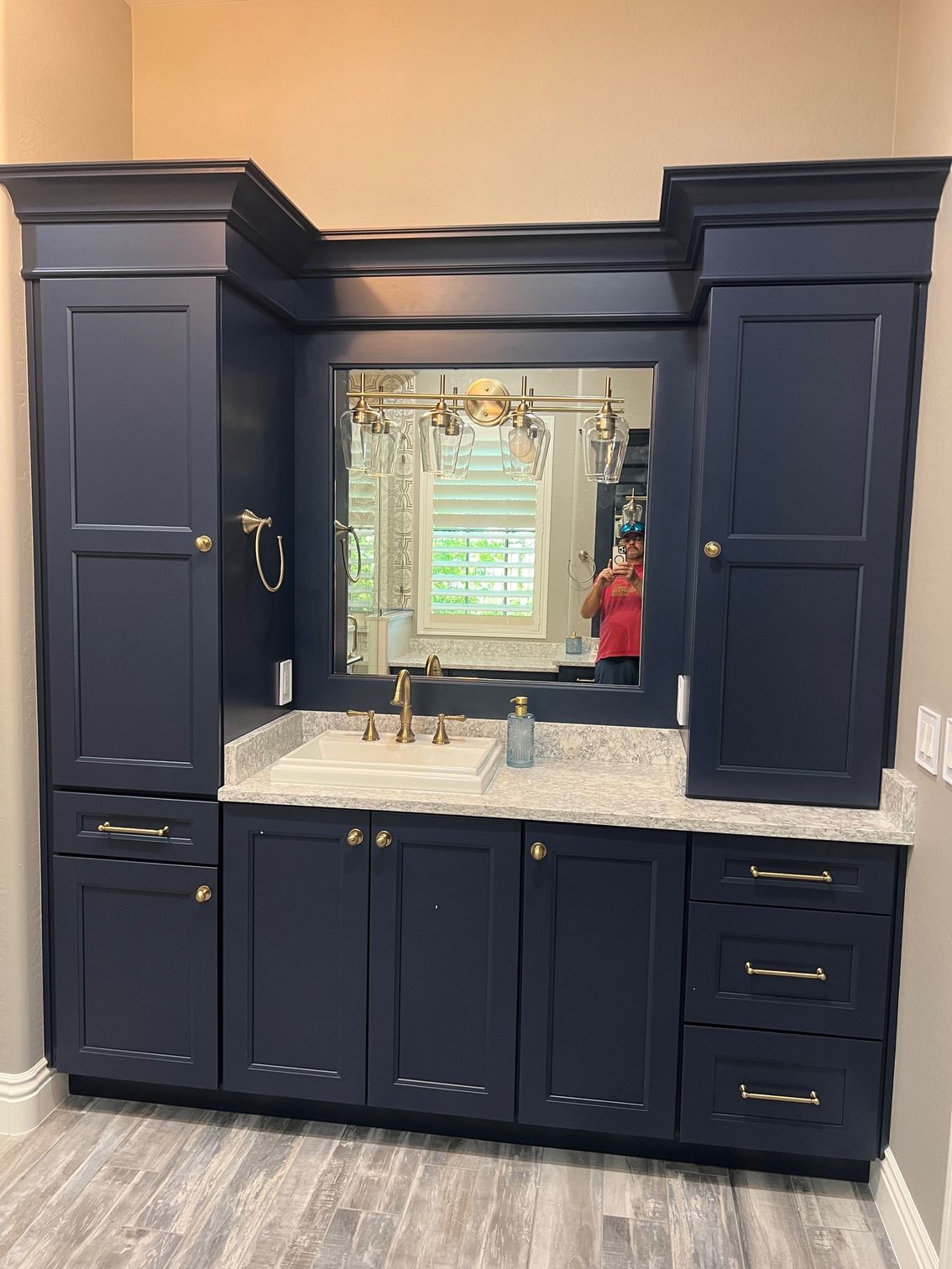 Dark navy bathroom vanity with mirror, white countertop, and brass hardware under wall cabinets.