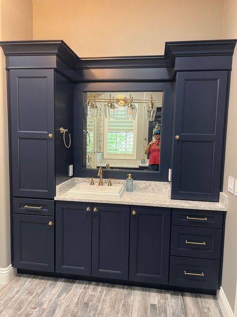 Navy bathroom vanity with marble countertop, large mirror, and cabinet storage against beige walls.