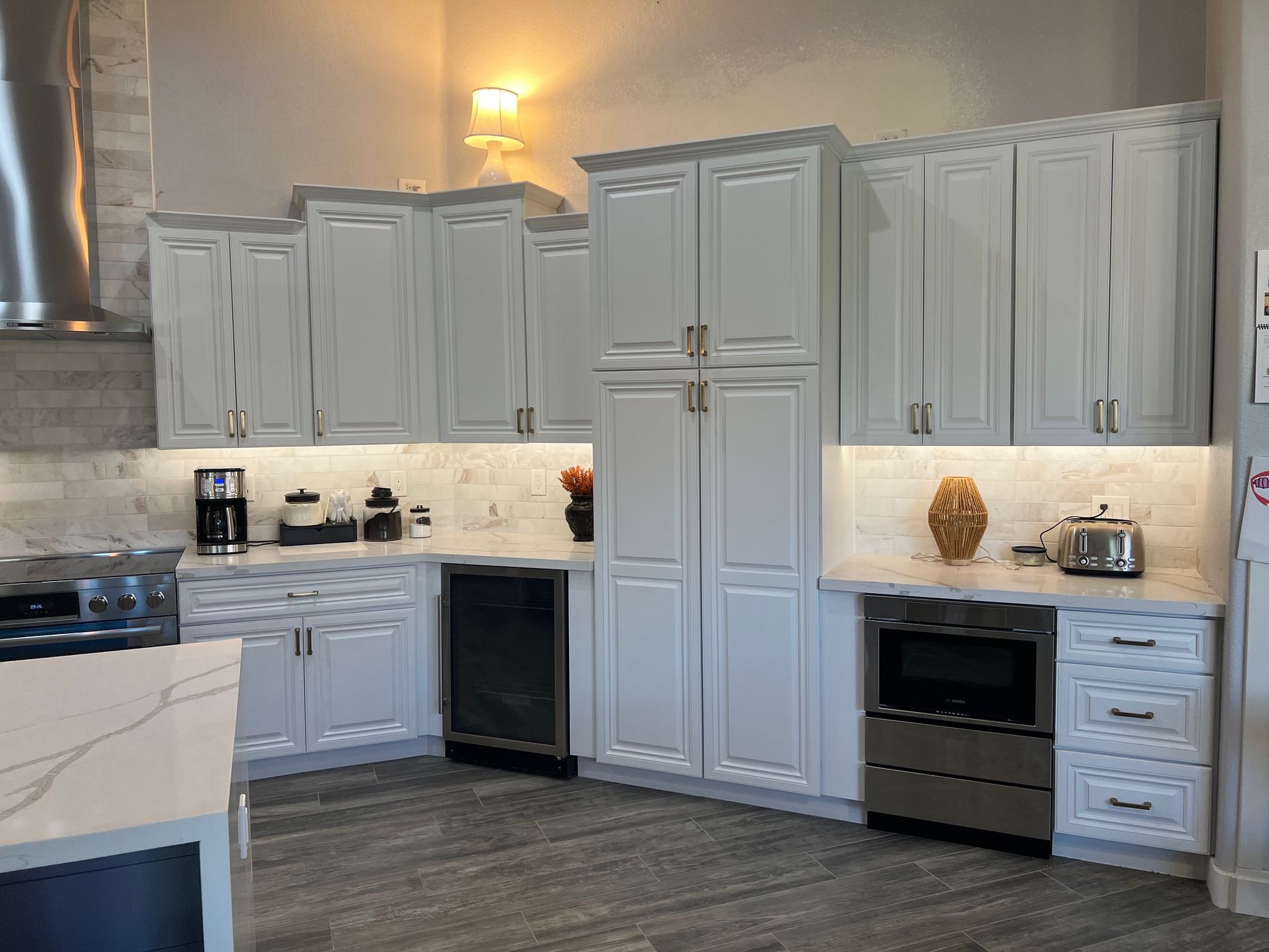 Modern kitchen with gray cabinets, white backsplash, stainless appliances, and wood-look floor.