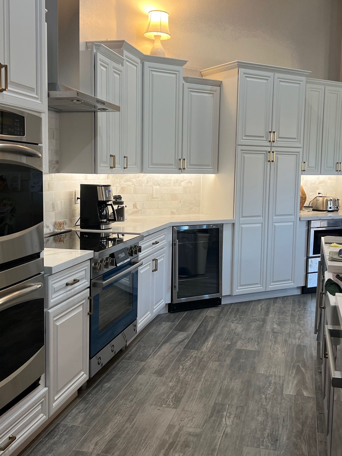 Modern kitchen with white cabinets, stainless steel appliances, and gray wood flooring