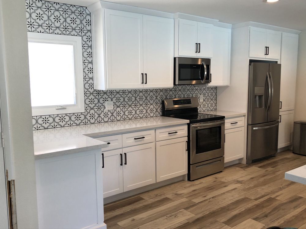 Bright modern kitchen with white cabinets, patterned backsplash, stainless steel appliances, and wood-look flooring