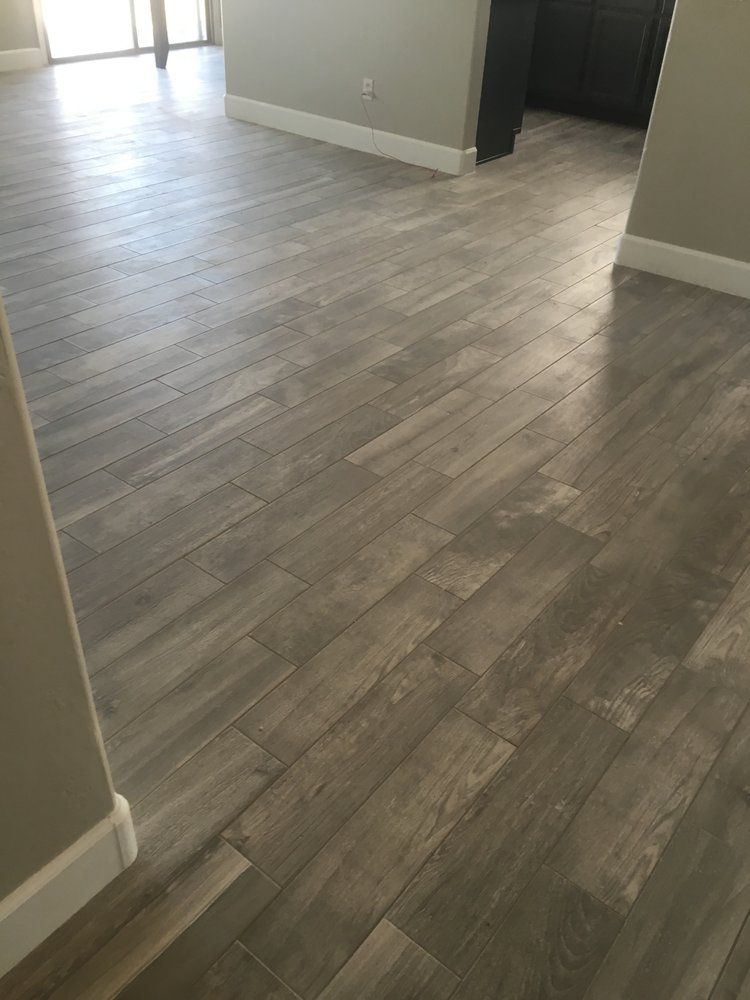 Empty room with gray wood-look flooring and white walls, viewed toward a bright doorway.