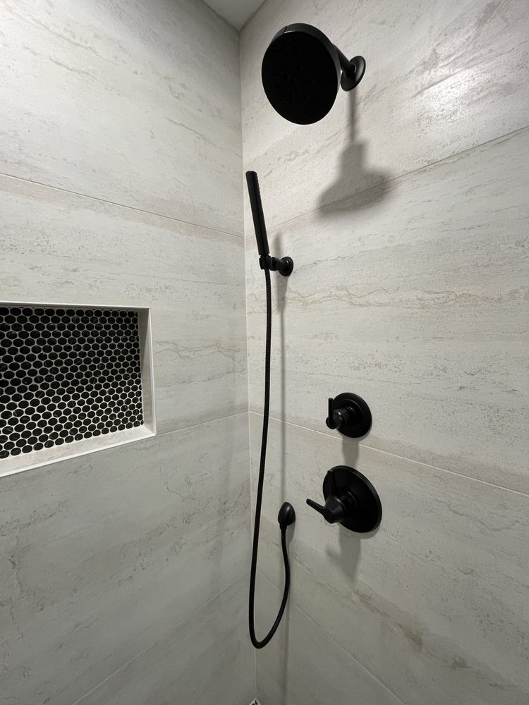 Shower stall with handheld showerhead, black fixtures, and a small ventilation opening.