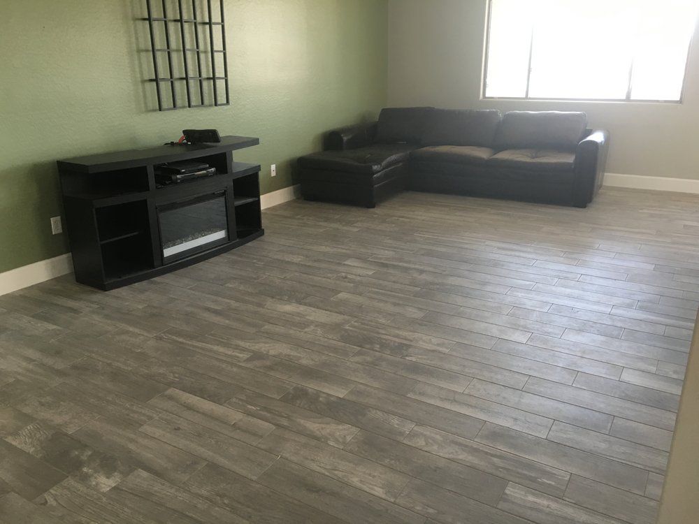Empty living room with gray wood flooring, black TV stand, and dark sectional sofa by a window.