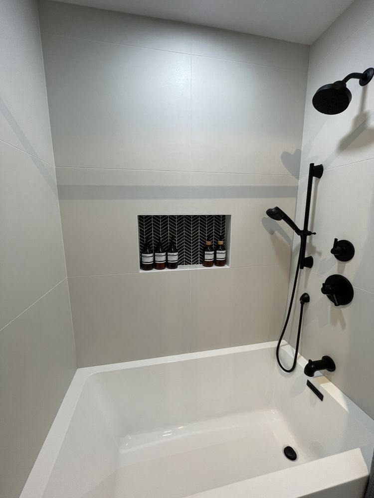 White shower/tub with black shower fixtures and built-in niche holding toiletries.