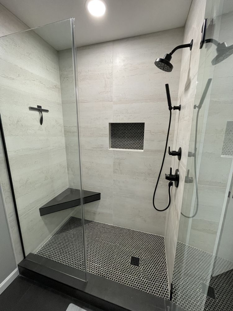 Modern walk-in shower with glass walls, black fixtures, built-in bench, and pebble-style shower floor.