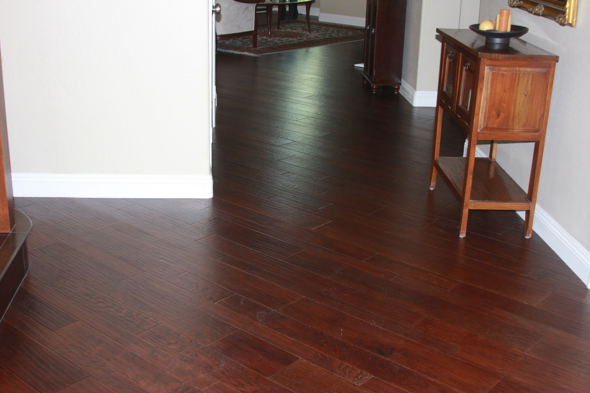 Empty room with dark hardwood floors and a small wooden side table along the wall