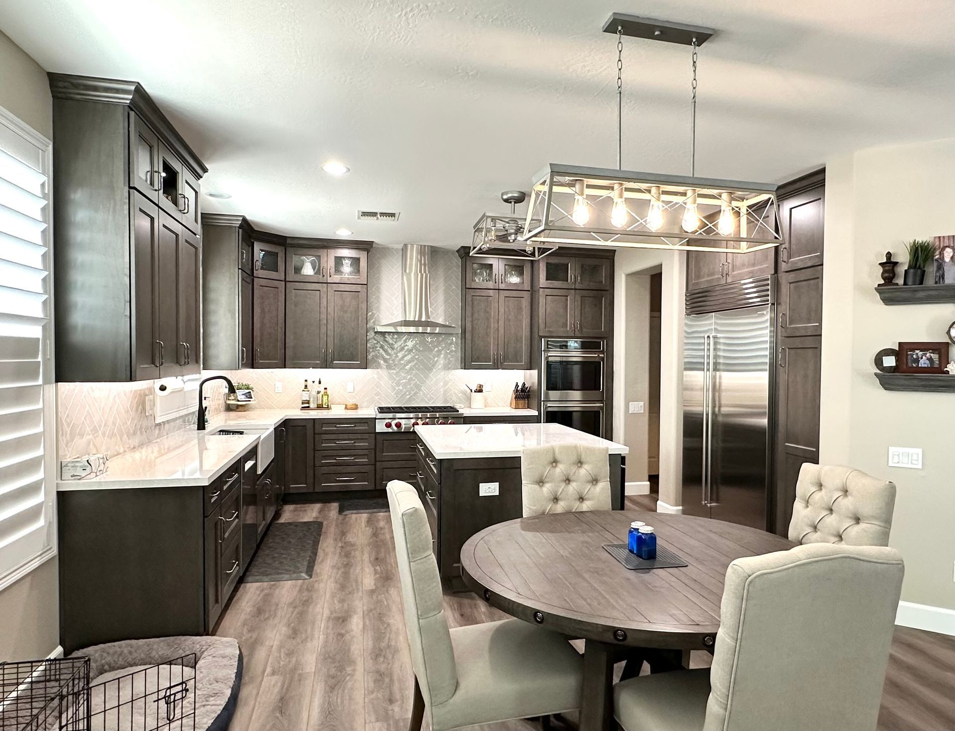 Bright modern kitchen and dining area with dark cabinets, white countertops, stainless appliances, and round table