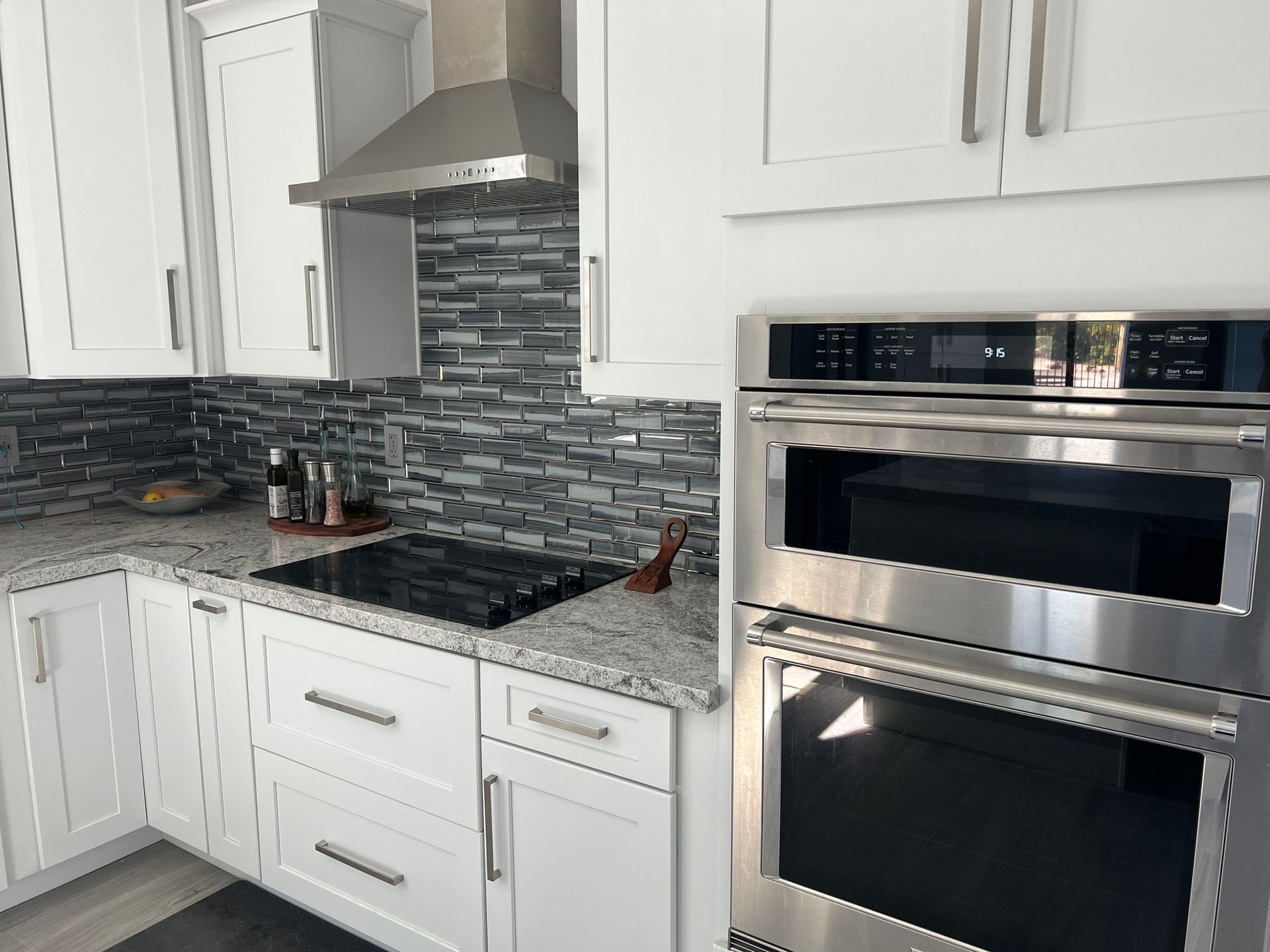 Modern white kitchen with gray tile backsplash, granite counters, and stainless steel built-in oven and microwave